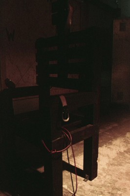 An electric chair at the center of the room helps set the mood.